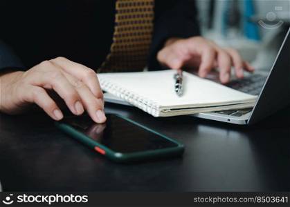 Businessman touching mobile smart phone digital internet technology network with computer laptop and pen book on desk.