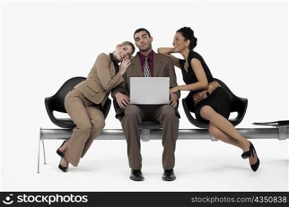 Businessman using a laptop and two businesswomen leaning on his shoulders