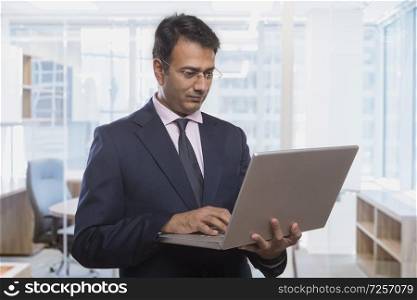 Businessman using a laptop holding in hand while standing in office
