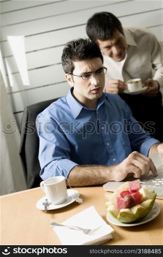 Businessman using a laptop with another businessman standing behind him