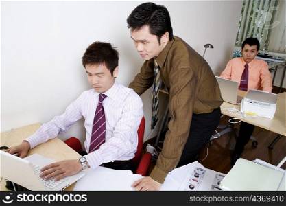 Businessman using a laptop with another businessman standing behind him