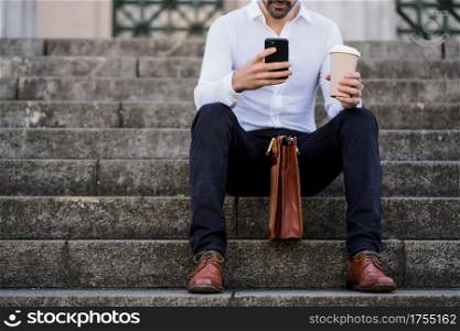 Businessman using a mobile phone while sitting on stairs outdoors. Business concept.