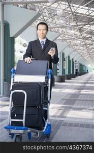 Businessman using a palmtop and pushing a luggage cart