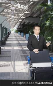 Businessman using a palmtop and pushing a luggage cart