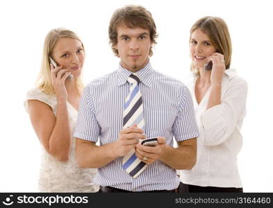 Businessman using a personal data assistant with two businesswomen using mobile phones