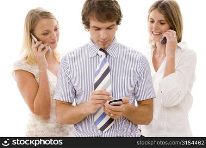 Businessman using a personal data assistant with two businesswomen using mobile phones