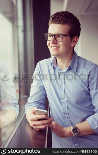 businessman using a phone beside window of modern office