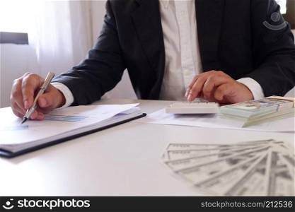 Businessman using calculator with money on the desk 