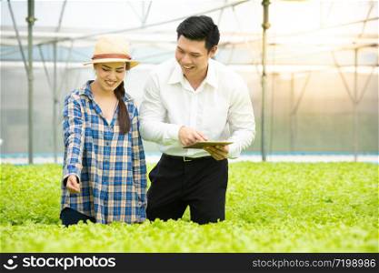 Businessman using digital tablet with 5g technology system check quality of hydroponic organic vegetable farm with asian beautiful woman farmer in greenhouse, business healthcare and medicine concept.