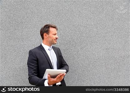 Businessman using electronic tablet leant against wall