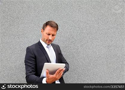 Businessman using electronic tablet leant against wall