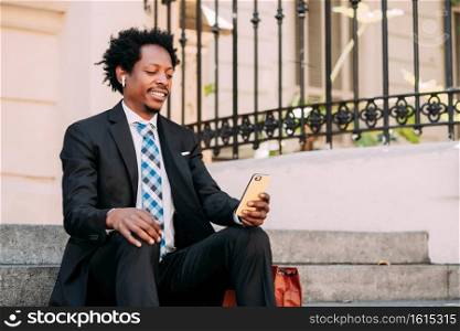Businessman using his mobile phone while sitting on stairs outdoors. Business and urban concept.
