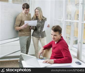 Businessman using laptop while coworkers discussing over documents in office