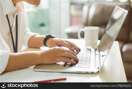 Businessman using laptop with tablet and pen on white table in office with a cup of coffee,side view and selected focus.