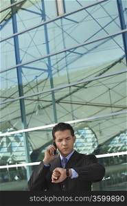 Businessman using mobile phone and checking watch outside office building