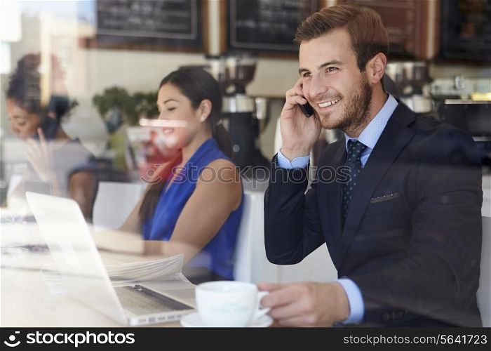 Businessman Using Mobile Phone And Laptop In Coffee Shop