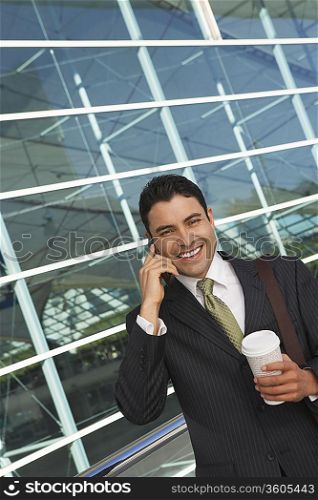 Businessman using mobile phone with take away coffee outside office building