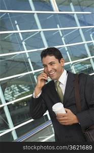 Businessman using mobile phone with take away coffee outside office building