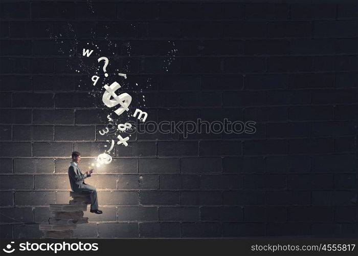 Businessman using mobile. Young businessman sitting on pile of books with mobile phone in hands