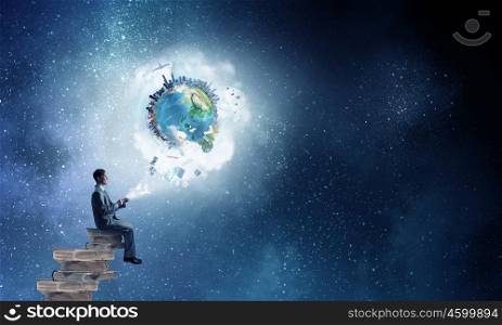 Businessman using mobile. Young businessman sitting on pile of books with mobile phone in hands. Elements of this image are furnished by NASA