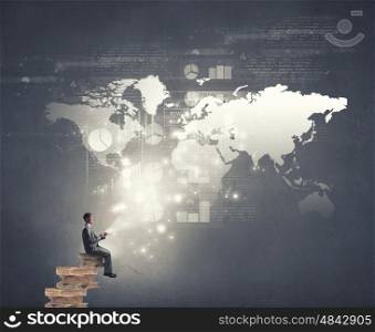Businessman using mobile. Young businessman sitting on pile of books with mobile phone in hands