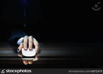 Businessman using mouse. Hand of businessman in suit on dark background using wireless computer mouse