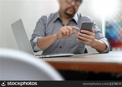 Businessman using smart phone for mobile payments online shopping with laptop computer on wooden desk in modern office 