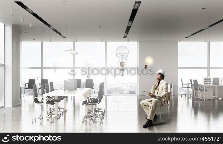 Businessman using tablet device. Elegant businessman in white suit sitting on chair in office interior