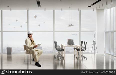 Businessman using tablet device. Elegant businessman in white suit sitting on chair in office interior
