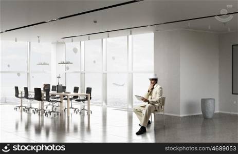 Businessman using tablet device. Elegant businessman in white suit sitting on chair in office interior