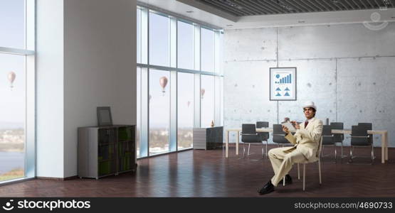 Businessman using tablet device. Elegant businessman in white suit sitting on chair in office interior