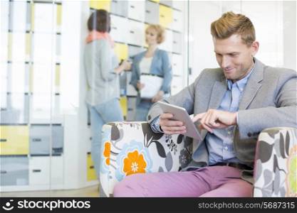 Businessman using tablet PC with colleagues discussing in background at creative office