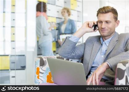 Businessman using technologies with colleagues discussing in background at creative office