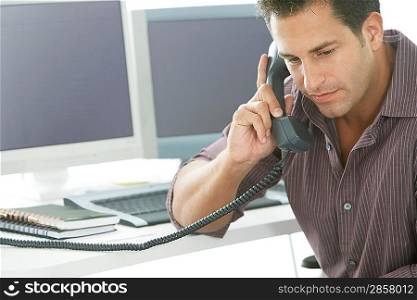 Businessman using telephone at desk in office