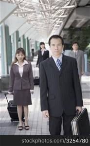 Businessman walking and holding his suitcase with three business executives in the background