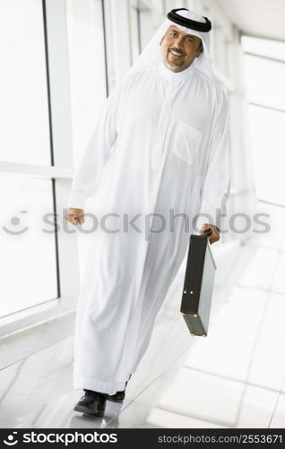 Businessman walking in a corridor with a briefcase smiling (high key/selective focus)