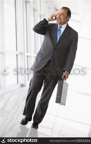 Businessman walking in corridor on cellular phone smiling (high key/selective focus)