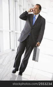 Businessman walking in corridor on cellular phone smiling (high key/selective focus)