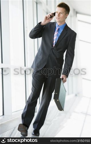 Businessman walking in corridor using cellular phone