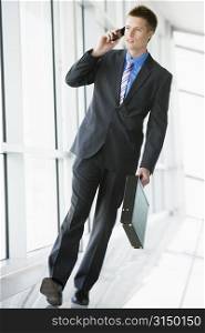 Businessman walking in corridor using cellular phone
