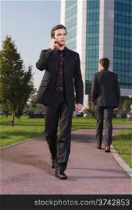 Businessman walking near office with mobie phone