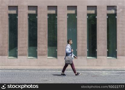 Businessman walking next to office buildings while holding a shoulder bag outdoors