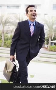 Businessman walking outdoors by building with a briefcase smiling (high key/selective focus)