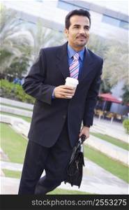 Businessman walking outdoors with coffee smiling (high key/selective focus)