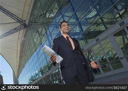 Businessman walking outside office building and smiling, low angle view