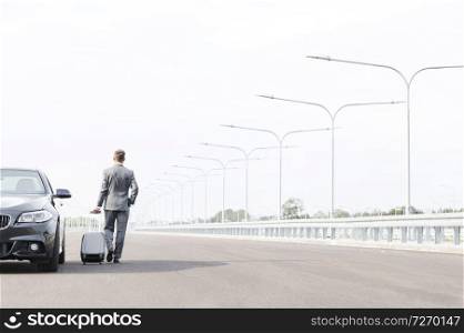 Businessman walking with suitcase by car on road against sky