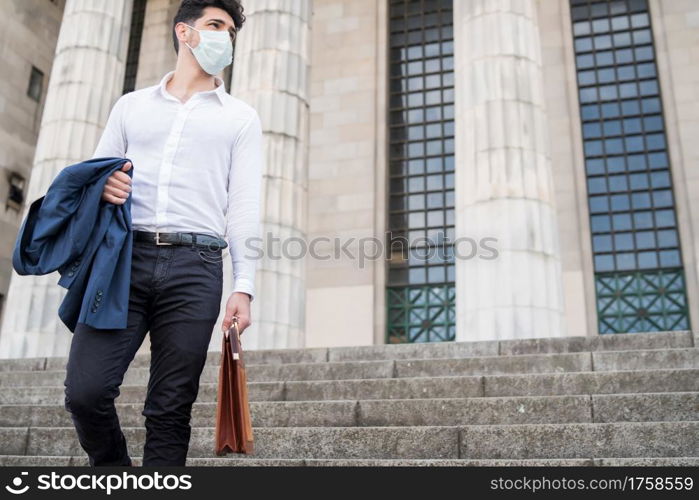 Businessman wearing a face mask and holding a briefcase while walking to work outdoors. New normal lifestyle. Business concept.