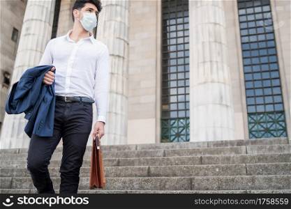 Businessman wearing a face mask and holding a briefcase while walking to work outdoors. New normal lifestyle. Business concept.