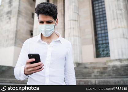 Businessman wearing a face mask and using his mobile phone while walking outdoors. New normal lifestyle. Business concept.