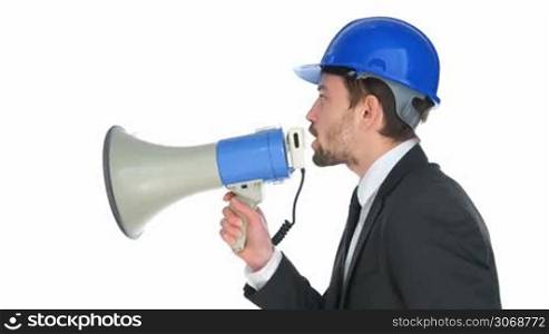 Businessman wearing a hardhat speaking into a megaphone as he makes a public announcement or issues instructions or a warning, side view on white
